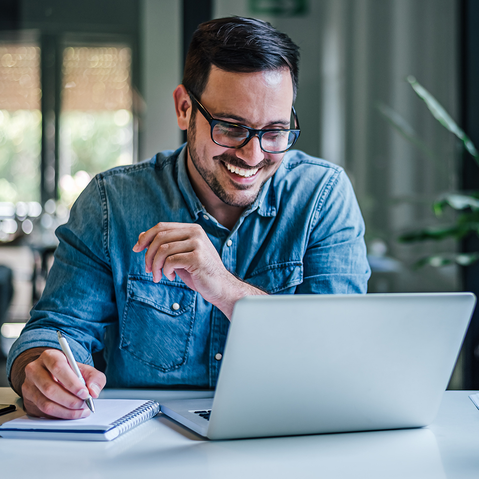 A man looking at a laptop and taking notes