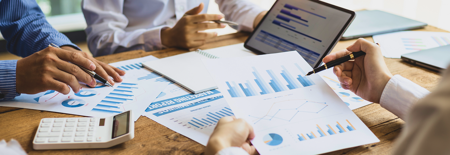 Close-up of three professionals examining graphs and charts on a wood table.