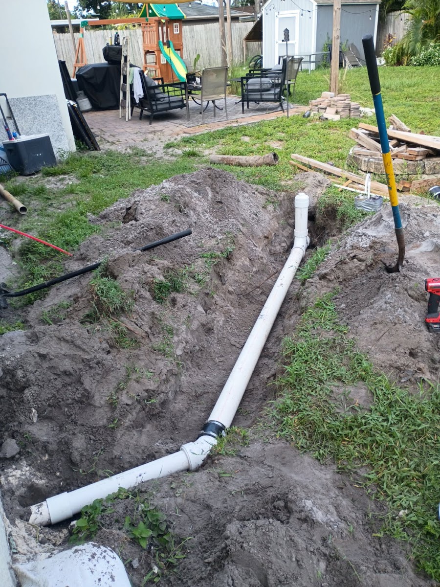 Underground plumbing line installation in progress, with exposed piping placed in a trench for an exterior water or drainage project.