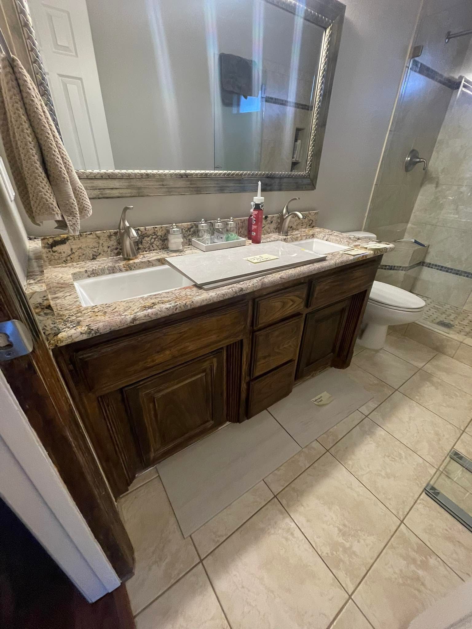 Bathroom remodeling project featuring a double vanity, granite countertop, wooden cabinetry, framed  