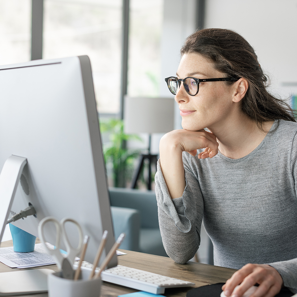 A woman sitting at a desk looking at a computer monitor