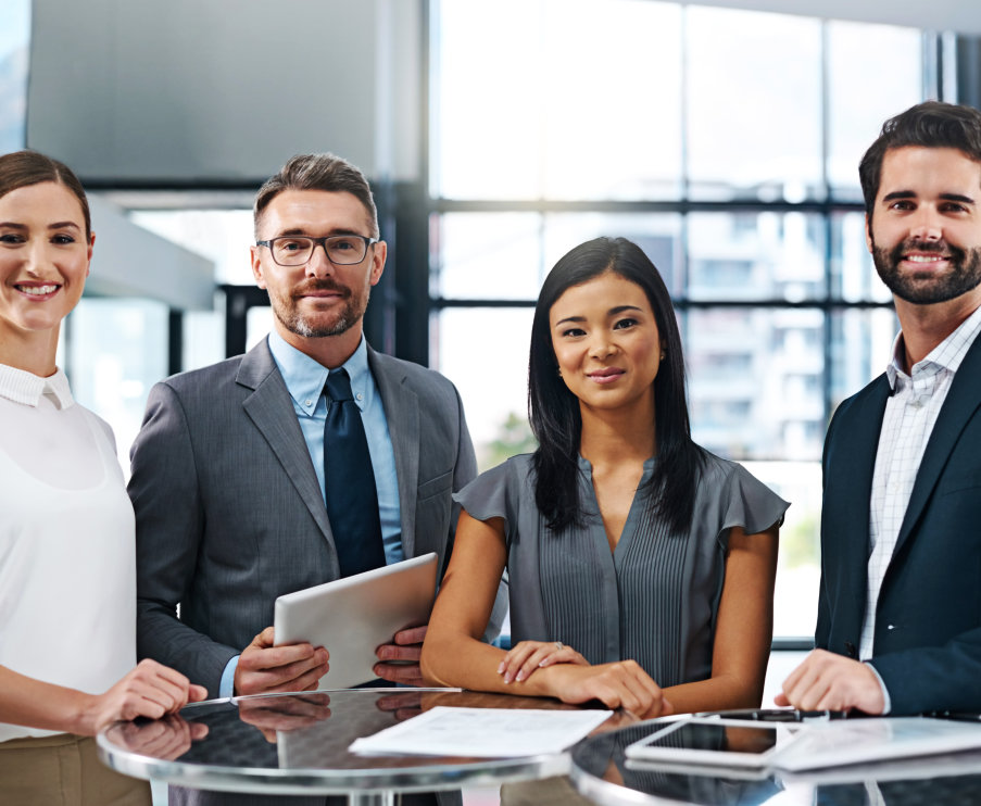 A diverse group of four business professionals, two women and two men, are standing around a reflect 