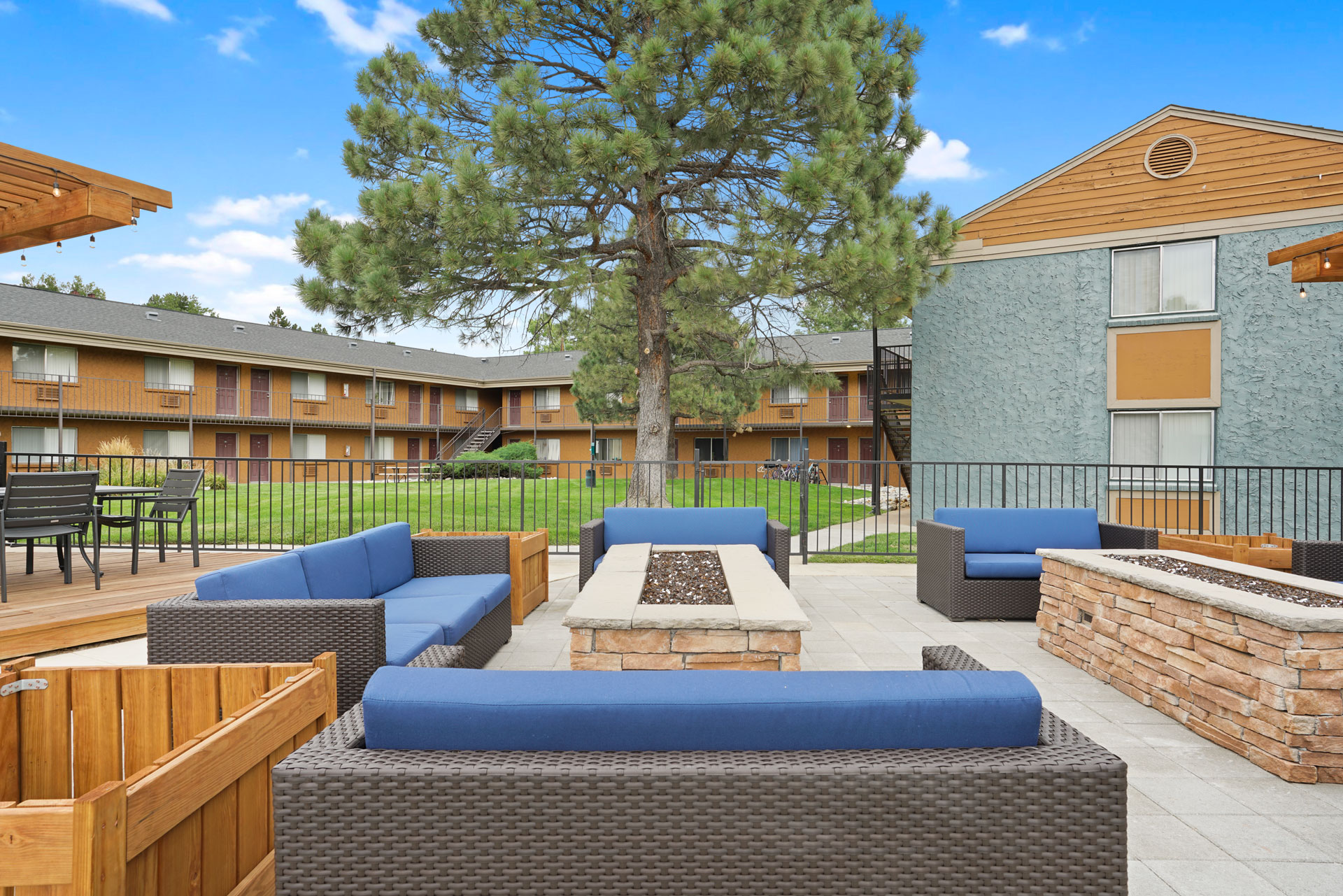 A large tree is in the middle of a patio with blue couches and wooden tables.
