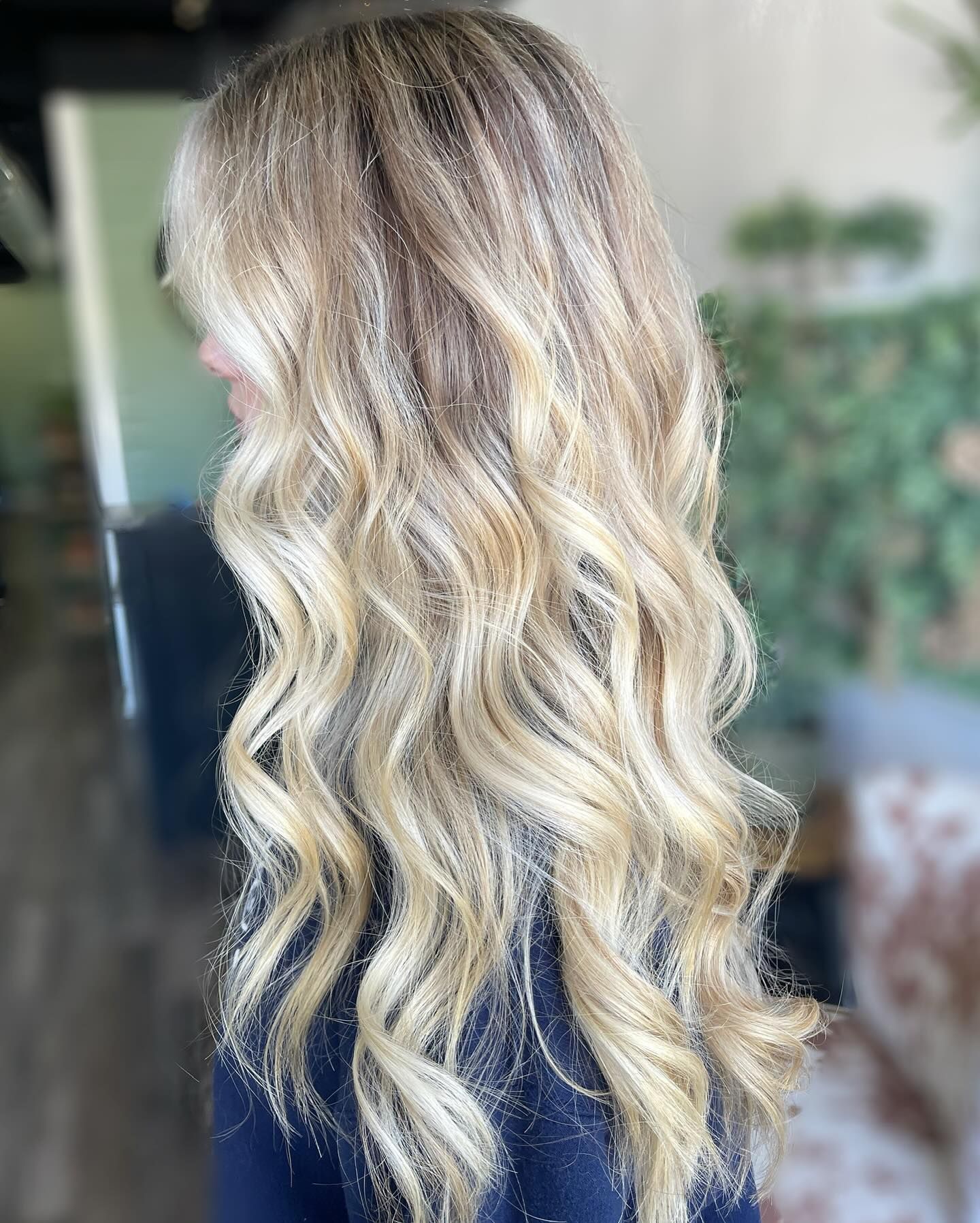 Side view of long blonde balayage hair styled in loose waves, blending darker roots into bright blonde ends beautifully.