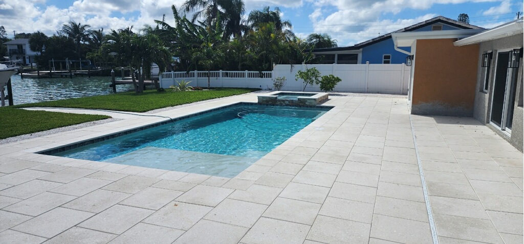 Newly finished residential swimming pool with a spacious light-colored deck and waterfront views.
