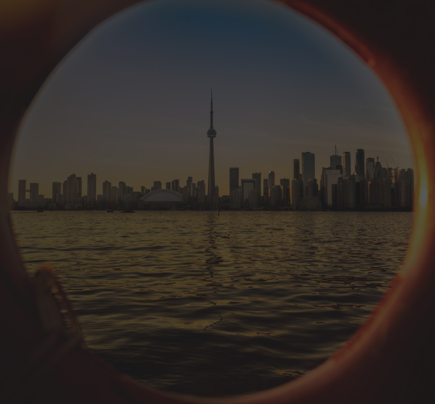 The Toronto skyline at sunset, seen from across Lake Ontario and pictured through an orange lifebuoy.
