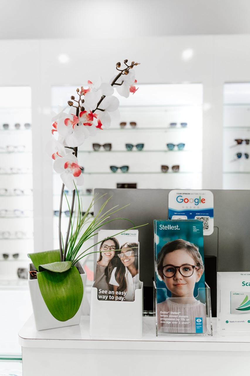 TK Optometry Brooklyn reception counter with decorative flowers, eyewear displays, and patient infor 