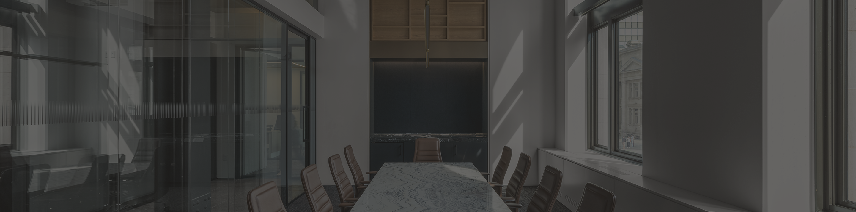 Sleek boardroom with large windows and a long marble conference table surrounded by brown leather chairs.