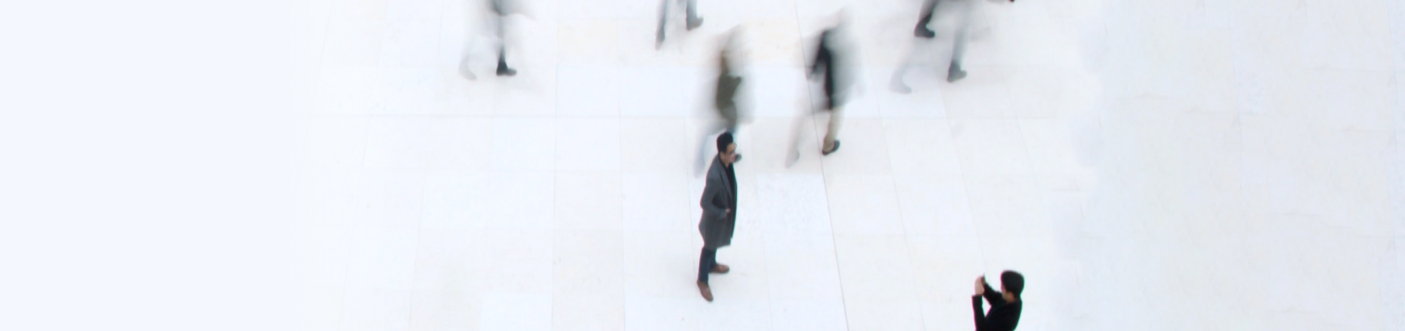 Overhead view of a man standing still in a busy public space as blurred figures walk past him.