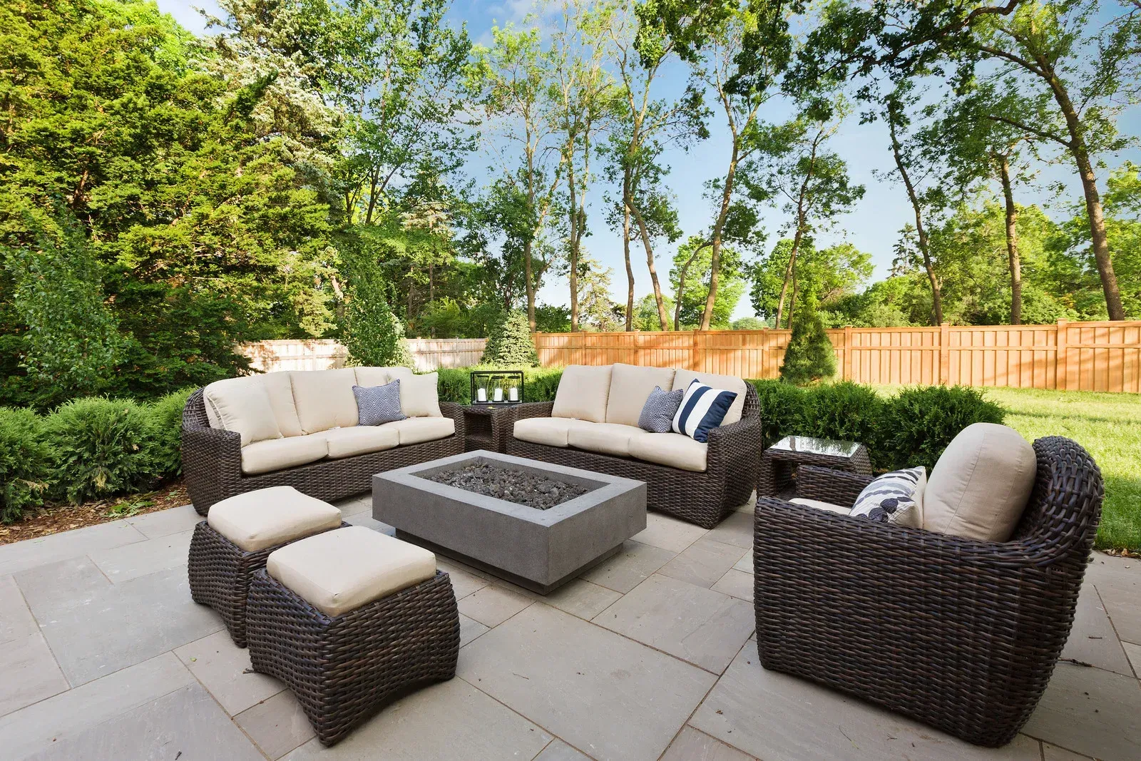Beautiful backyard patio featuring wicker seating, fire pit, landscaped shrubs, mature trees, and pr 