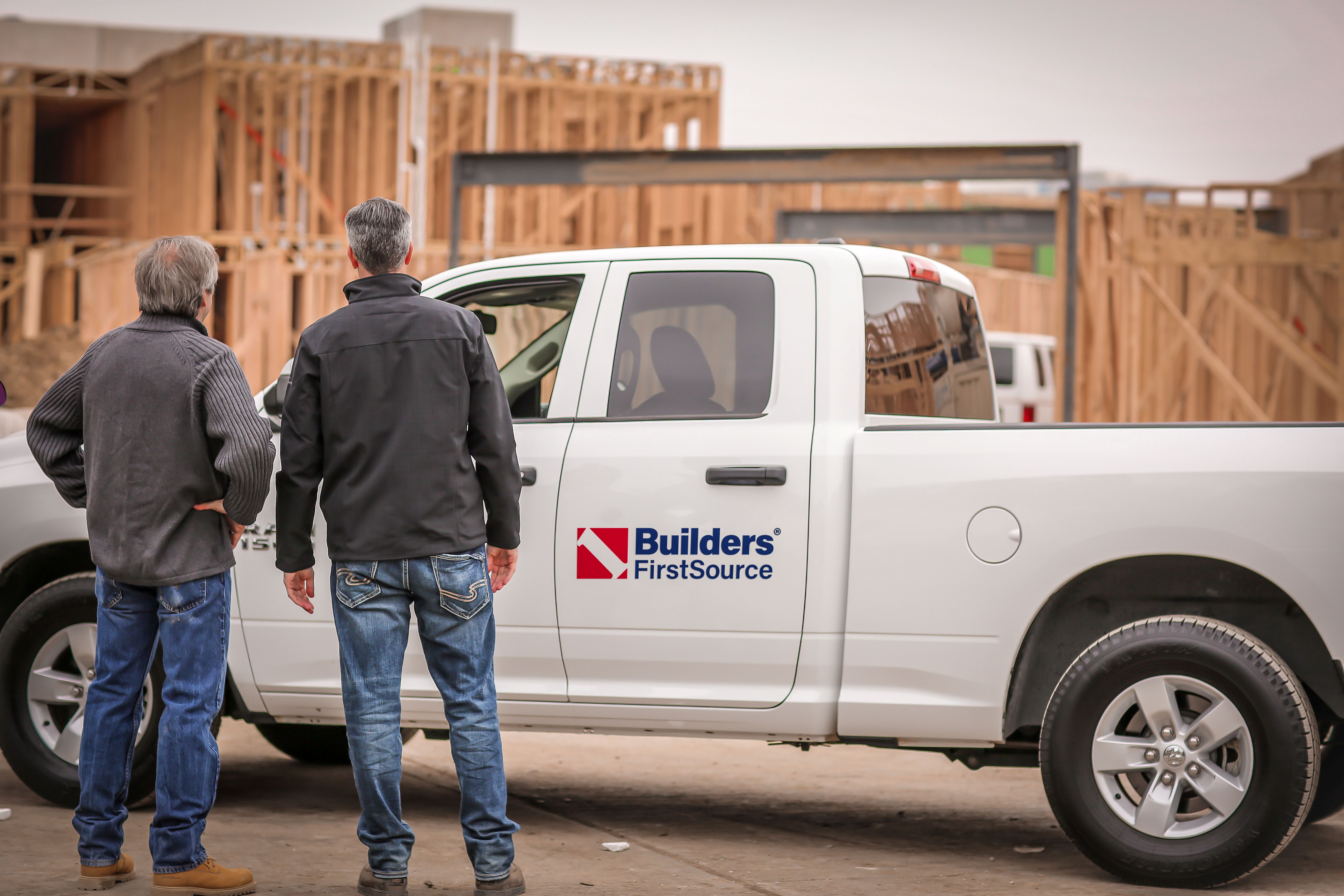 Customer speaking with a store associate at a retail hardware counter, with tools, equipment, and supplies displayed in the background, including ladders and product racks.