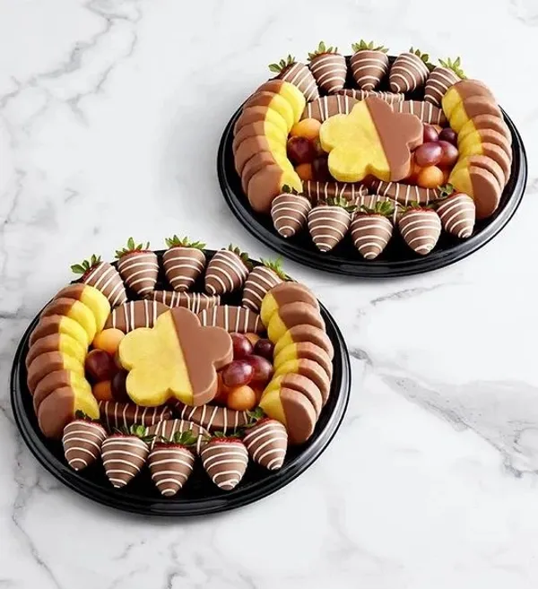 Two black platters are filled with a variety of fruits, including strawberries dipped in chocolate,  