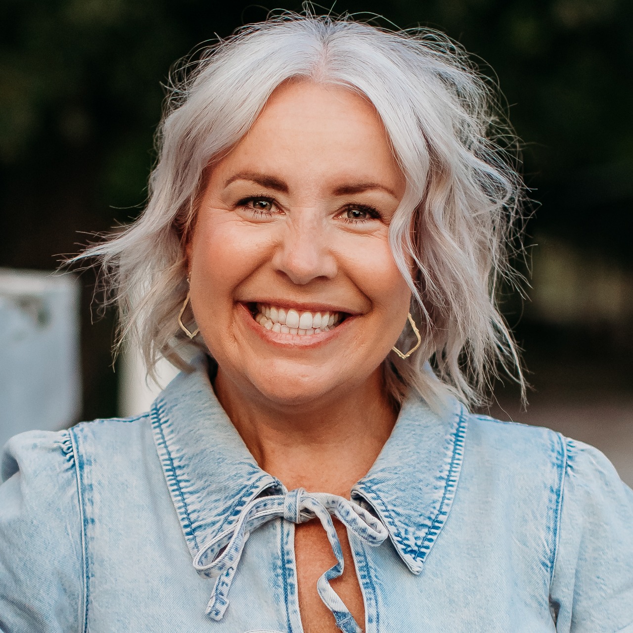Smiling founder of Agency Ten10 in a close-up outdoor portrait wearing a light denim top.