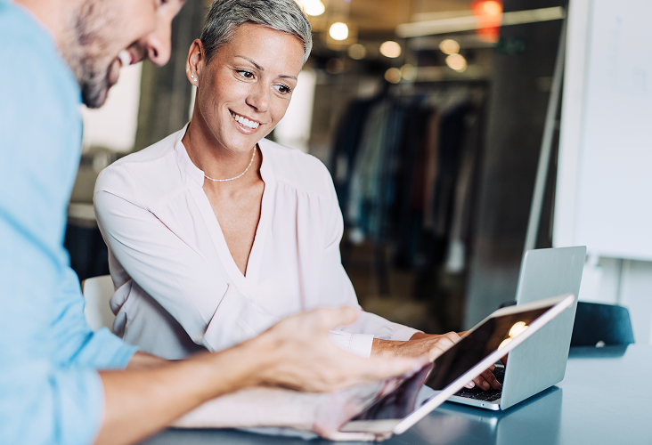 A short-haired woman talking to her financial advisor and looking down at his tablet.