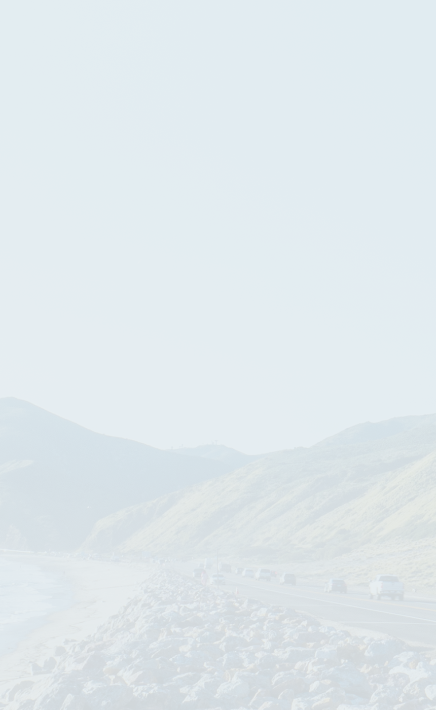 A seaside highway bordering mountains on the right and an ocean to the left.