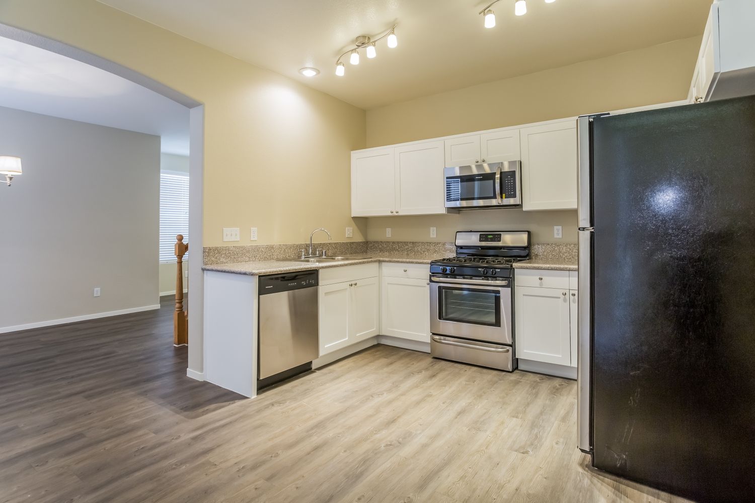 Kitchen with modern light fixtures, stainless-steel appliances, white cabinetry and luxury vinyl plank flooring at Invitation Homes Las Vegas.