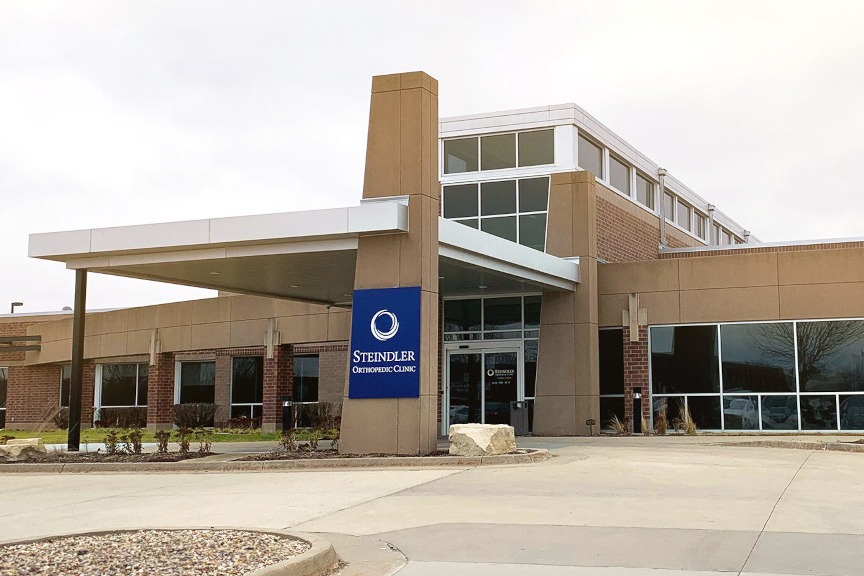 Exterior view of a modern medical facility with clear signage, featuring the main entrance and parking area of the Steindler Orthopedic Clinic building on a cloudy day.