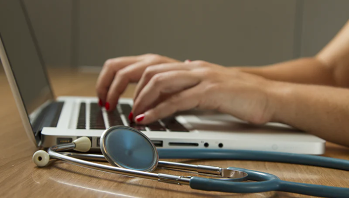 A stethoscope next to someone typing on their laptop.