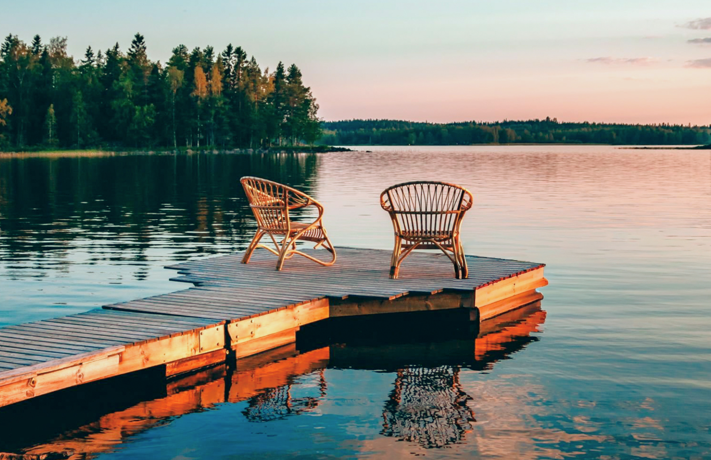 Two wooden chairs on a dock overlooking a lake at sunset.