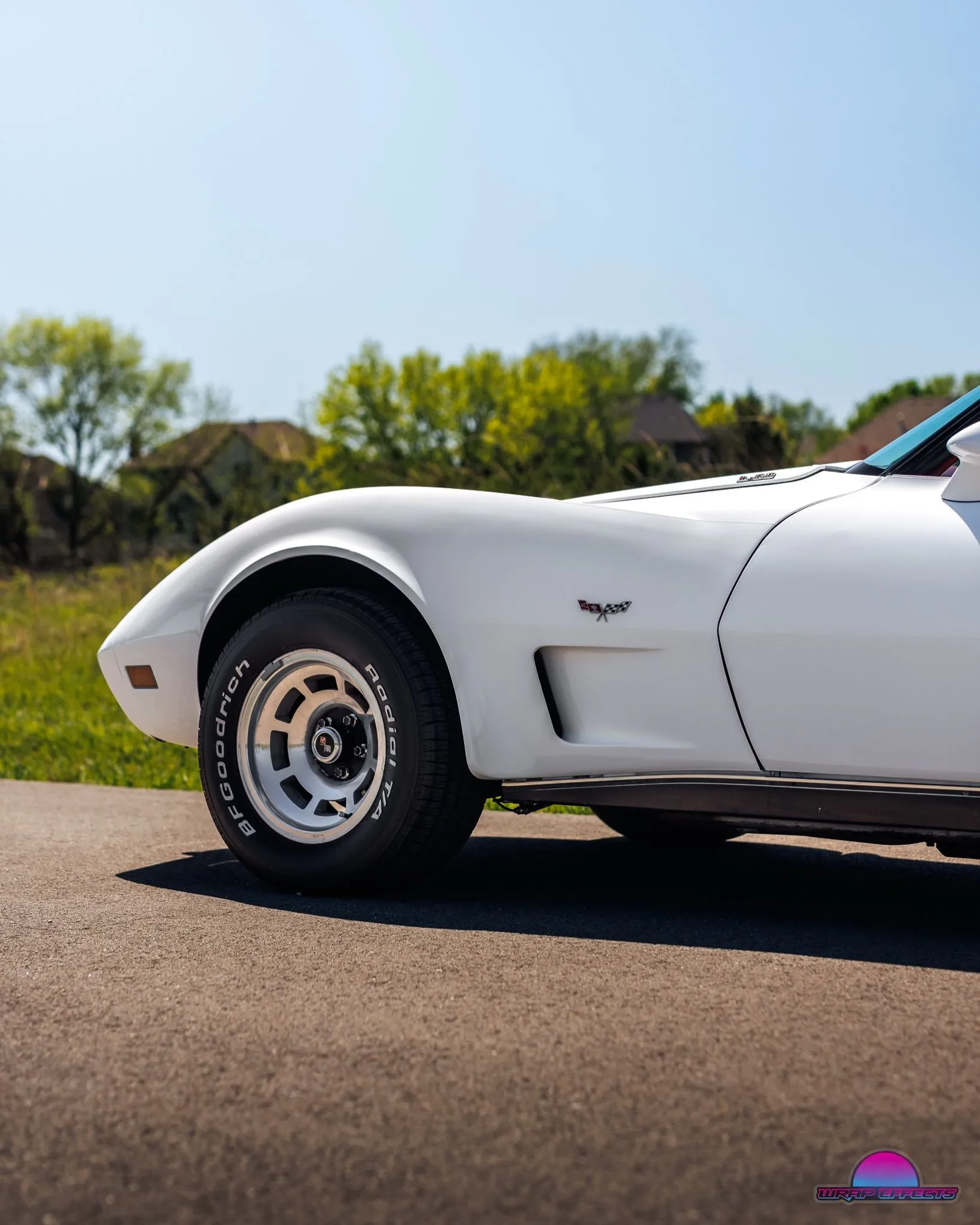 Close-up side profile of classic white Chevrolet Corvette highlighting sculpted fender, vintage styling, performance wheels, and iconic sports car design photographed under clear blue skies outdoors beautifully.