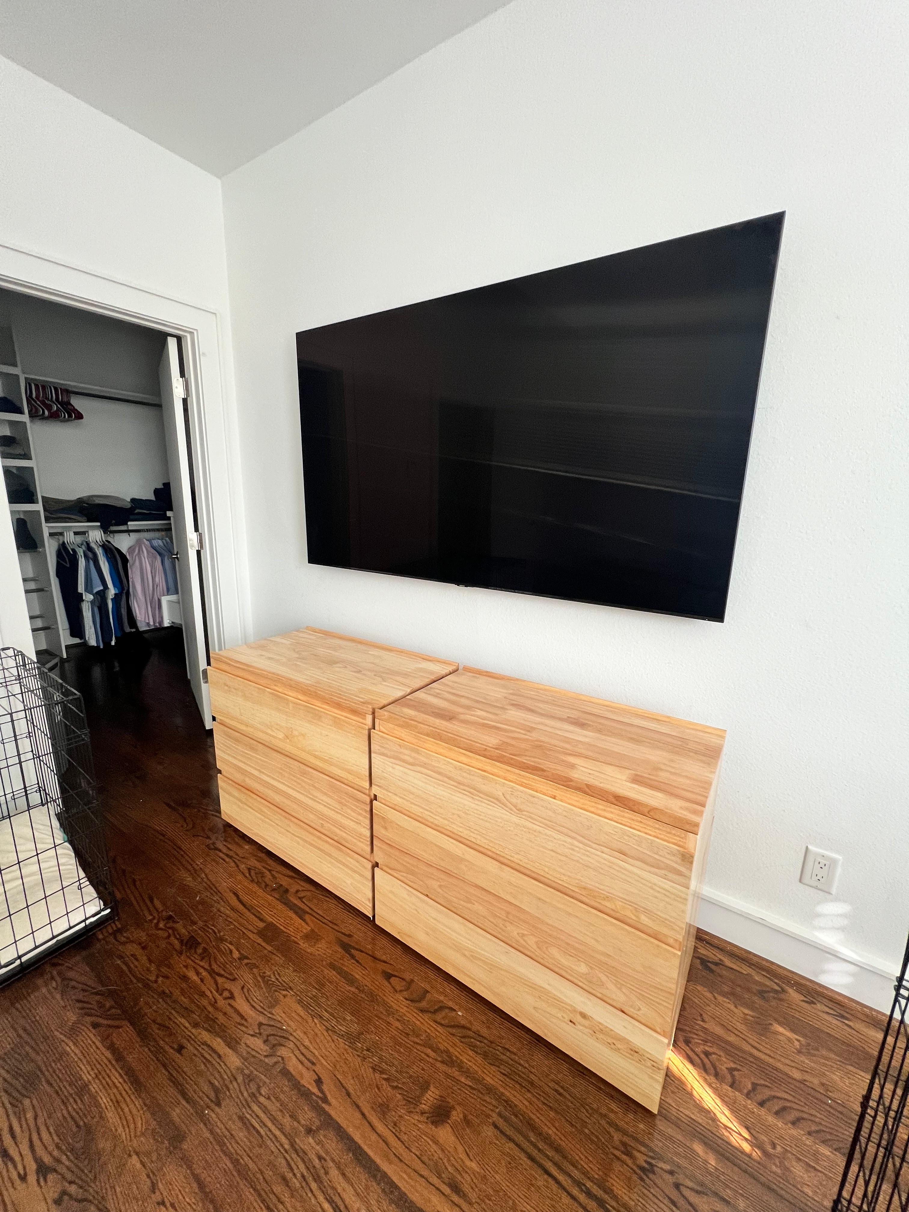Large flat-screen TV mounted on a bedroom wall above a wood dresser in a Houston home.