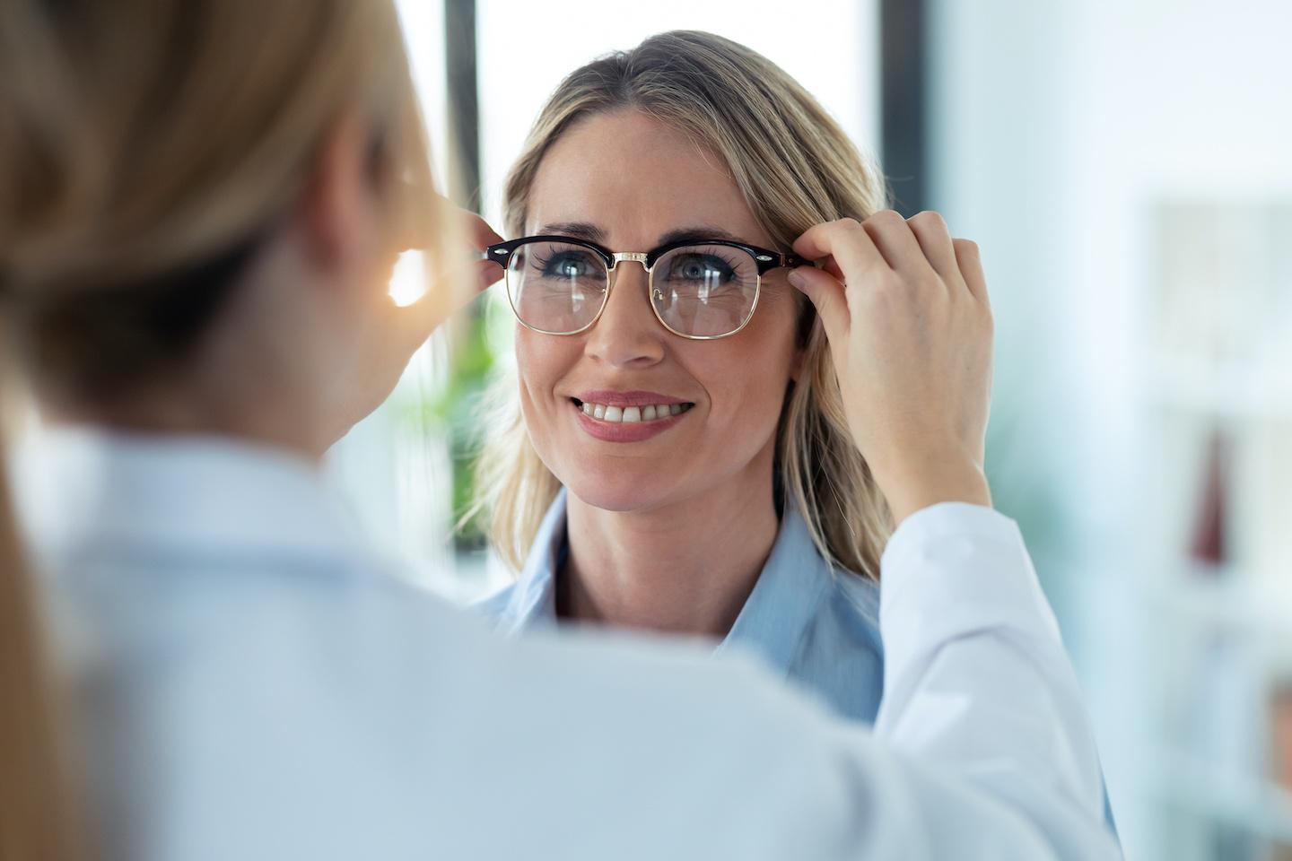 Optometrist placing a pair of glasses on a female patient.