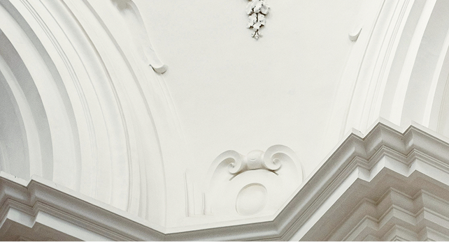 A white, arched ceiling in a grand building with a small window.