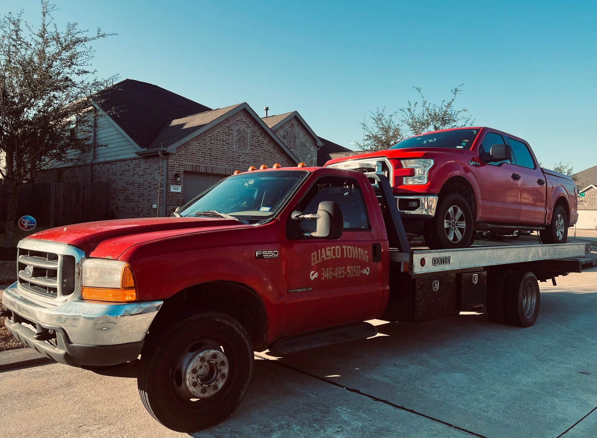 Eliasco Towing red flatbed truck transports a red pickup truck on its carrier in a residential neighborhood, showcasing professional vehicle towing and roadside transport services.