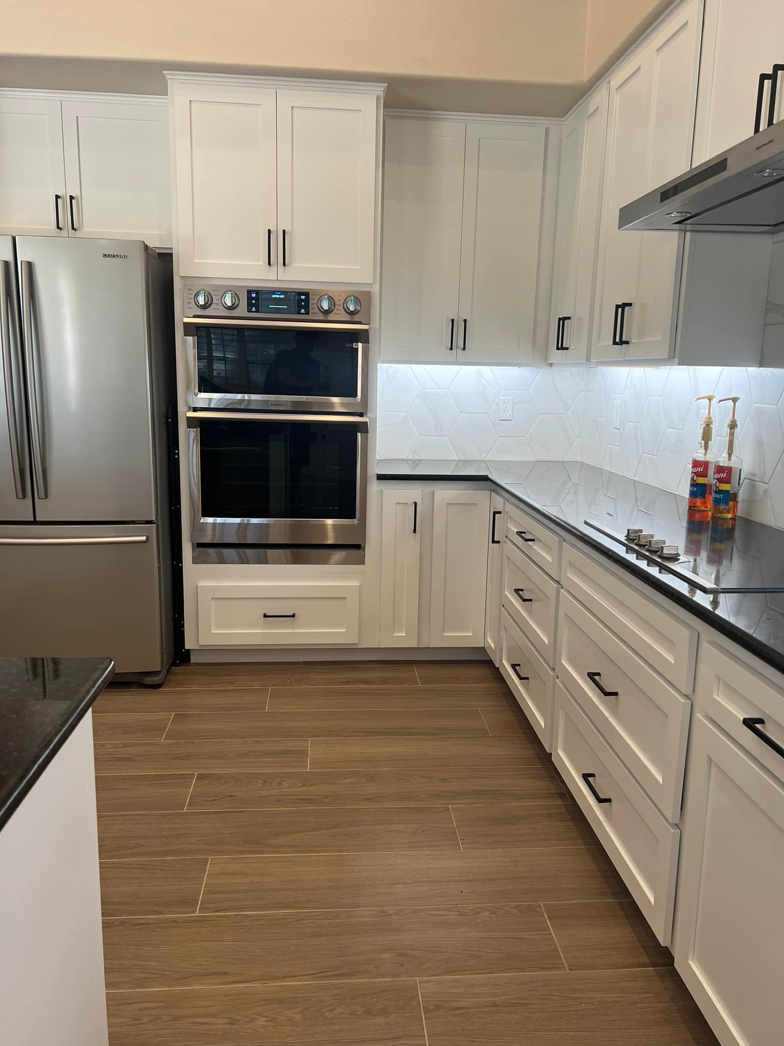 This modern kitchen features white shaker-style cabinets, dark countertops, and light brown wood-loo 