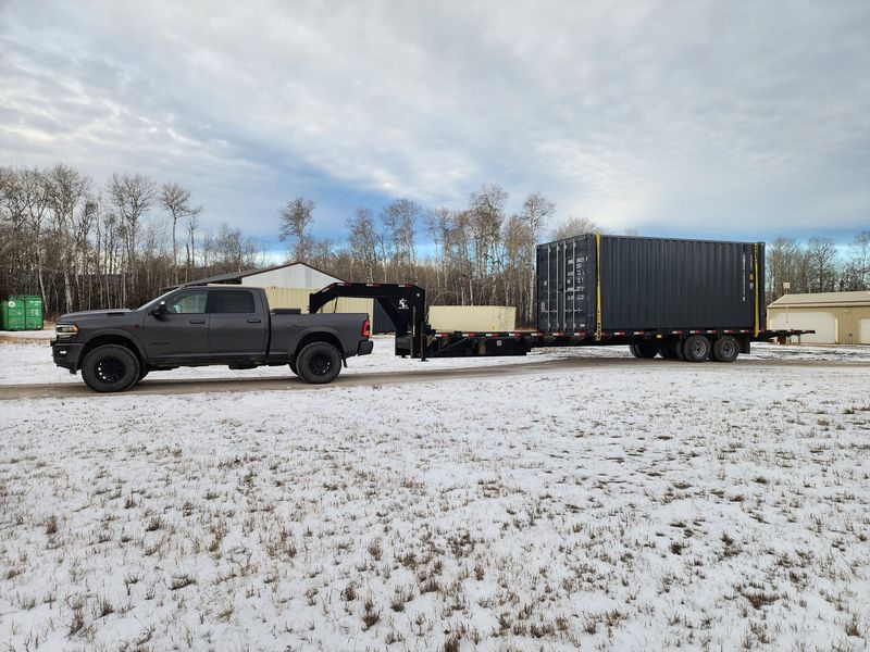 Pickup truck towing large portable storage container on flatbed trailer across snowy ground, demonstrating delivery service for secure storage units used in residential, commercial, or construction storage applications.