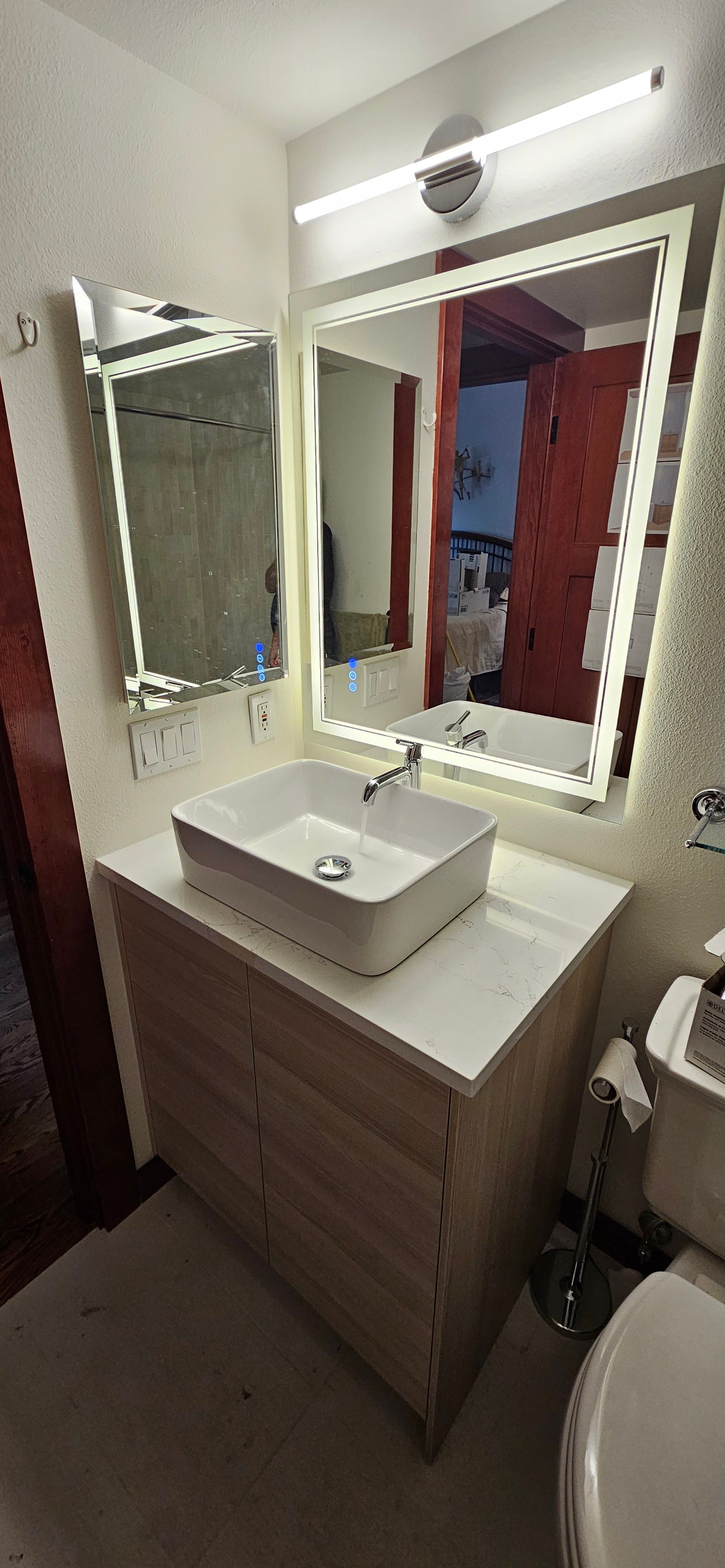 Modern bathroom vanity installation featuring a white vessel sink, chrome faucet, illuminated mirror 