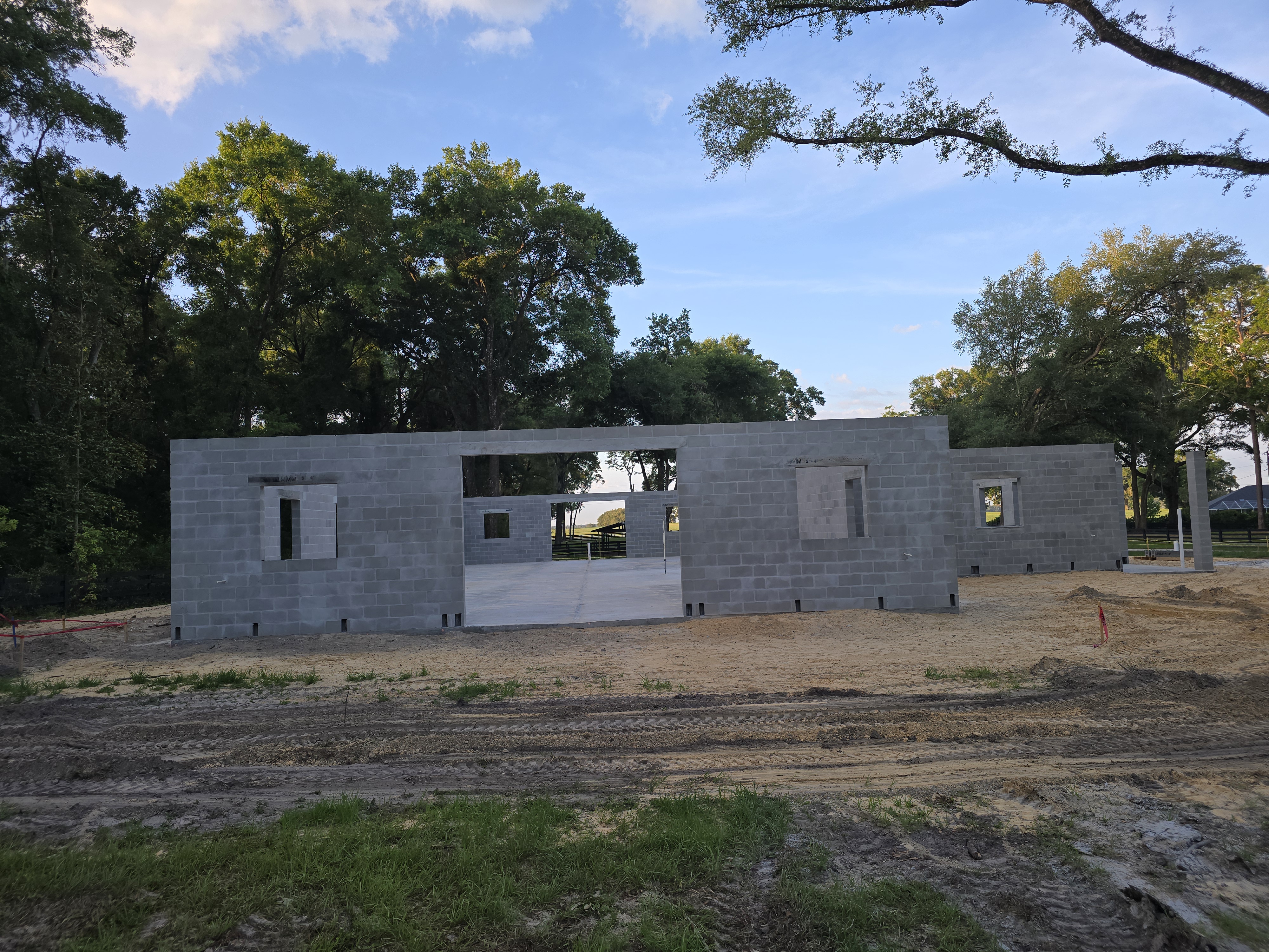 A construction site with a partially built cinder block structure under a blue sky with scattered cl 