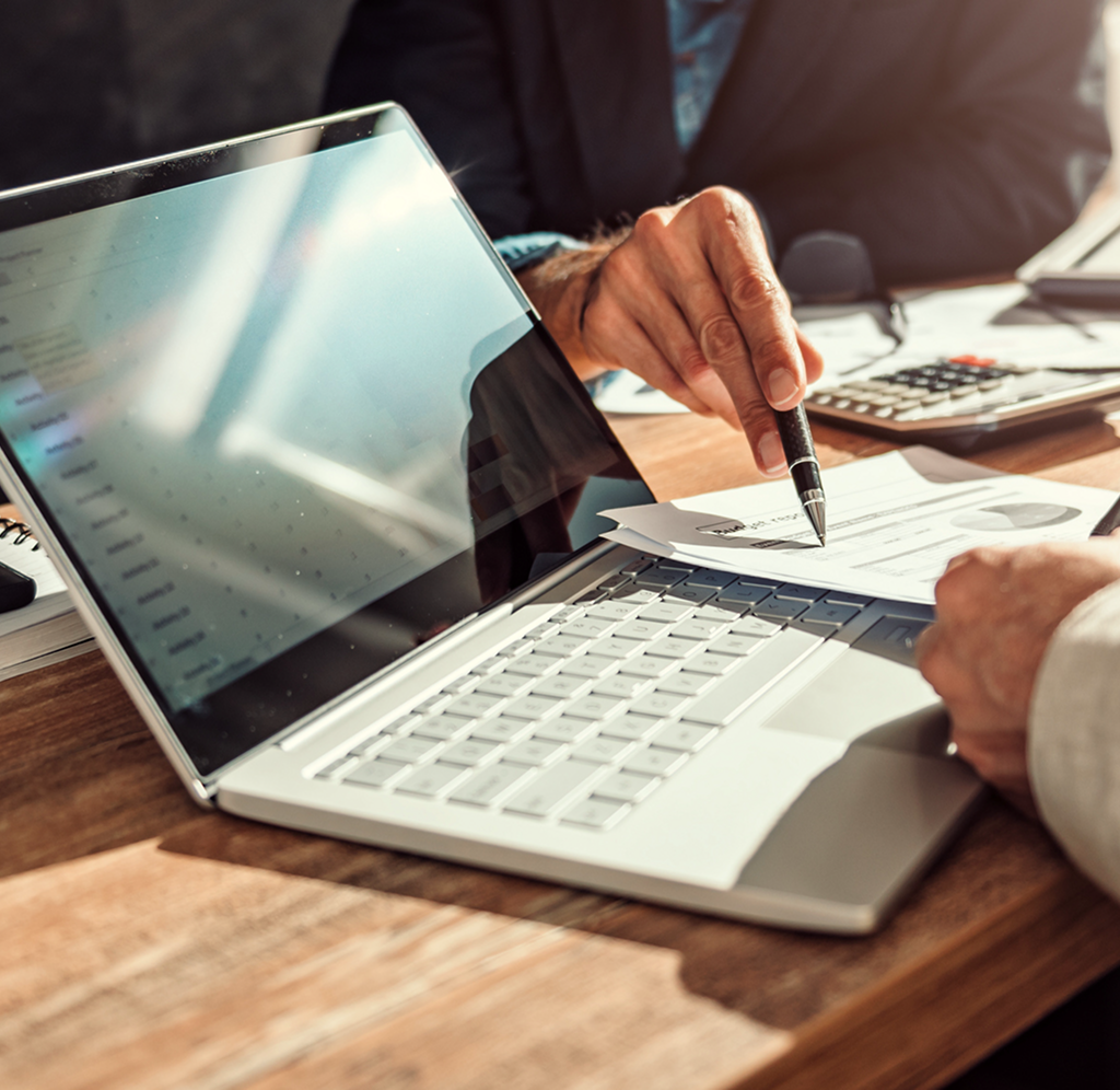 Two investment advisors collaborating at a desk with their notebooks and laptop.