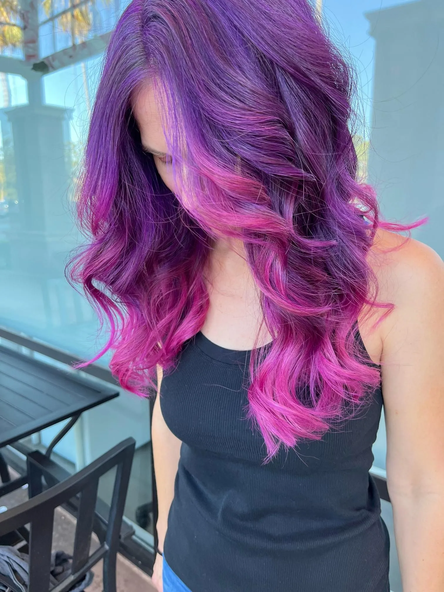 Vibrant purple and pink balayage hairstyle styled in soft flowing waves, creating bold color contrast and dimension. The look highlights creative salon hair coloring techniques and modern professional styling.