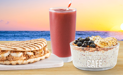 Peanut Butter Banana Crunch Flatbread, a purple Tropical Smoothie in a glass with a straw, and a Chia Seed Yogurt Bowl topped with blueberries and banana on the beach at sunset with the ocean in the background.