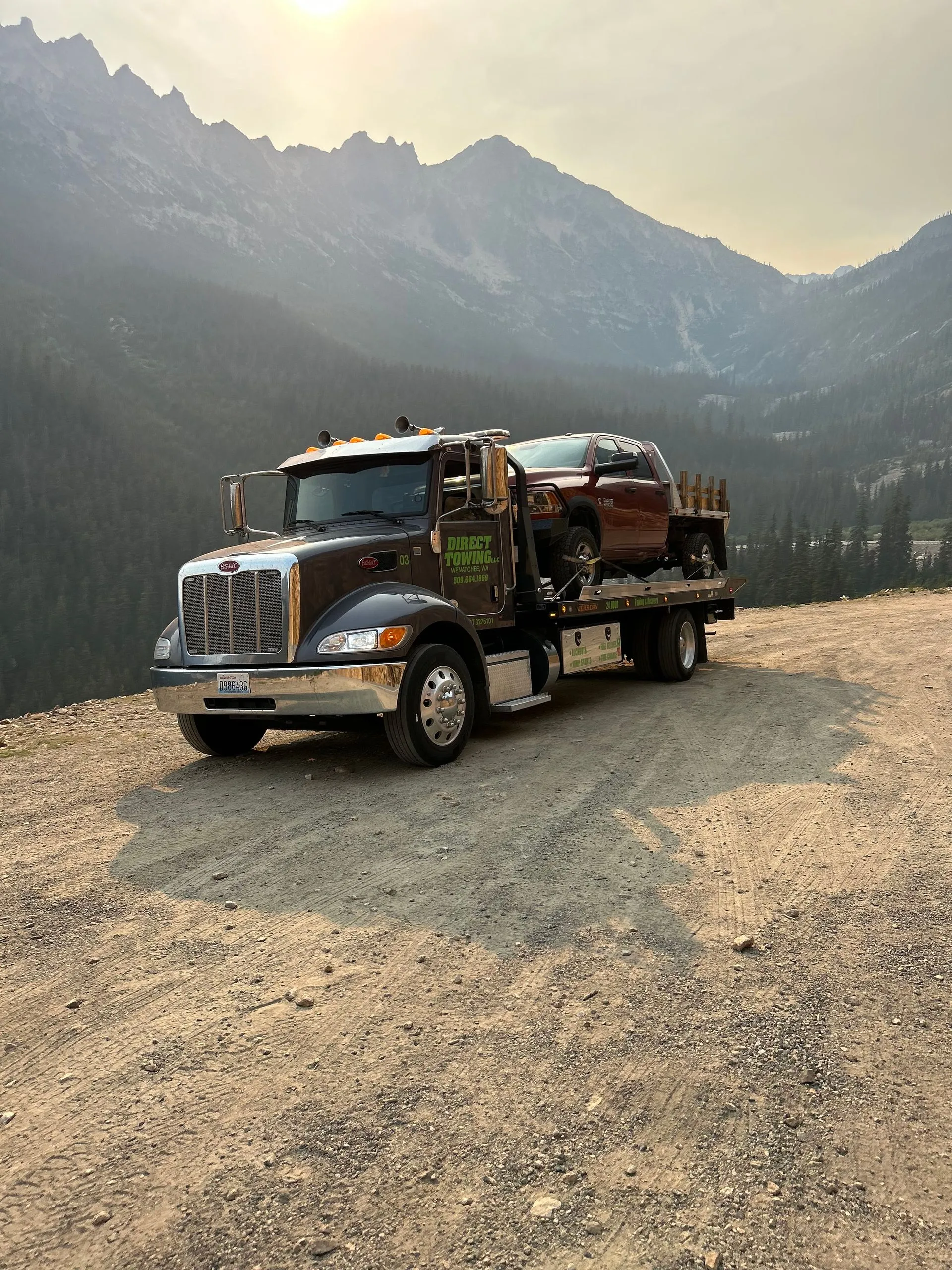 Heavy-duty Direct Towing flatbed transporting a pickup truck through a scenic mountain environment, demonstrating long-distance vehicle hauling, secure transport solutions, and reliable recovery services across challenging terrain.