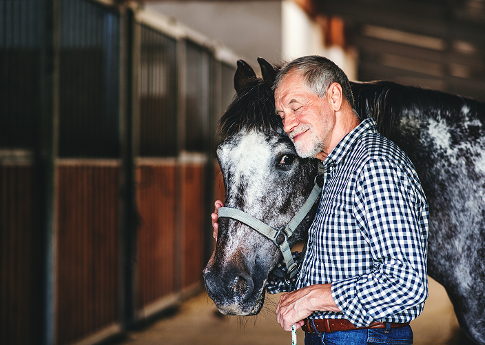 A man smiling while head to head with his horse.