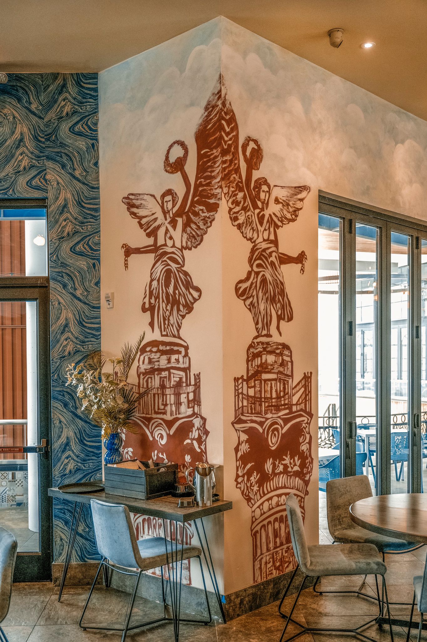 The blue accents on the wall create a calming effect, contrasting beautifully with the warm tones of the mural art. The corner feels intentional, adding a touch of sophistication to the dining experience.