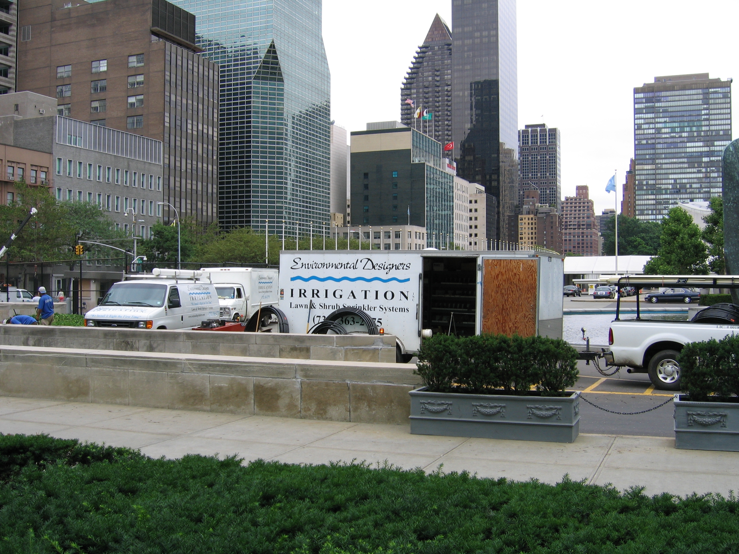 Commercial irrigation service trucks parked in a city plaza with urban skyscrapers in the background.