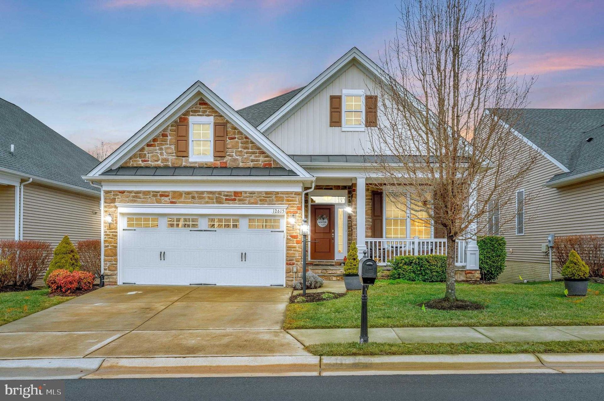 Charming suburban house with stone and siding exterior, front porch, driveway, landscaped lawn, and garage, representing practical and aesthetically pleasing residential construction for comfortable family living.