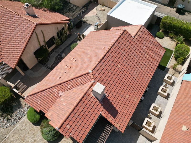 High-angle aerial drone view of a finished residential roofing project. The image highlights a clean, uniform installation of red clay barrel tiles on a suburban home with desert landscaping.