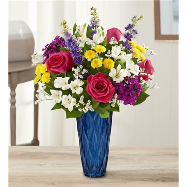 Set the scene for special moments with our stunning arrangement. A blend of jewel tone blooms is hand gathered in our Blue Harmony vase, adding striking color and exquisite texture to this luxurious surprise.