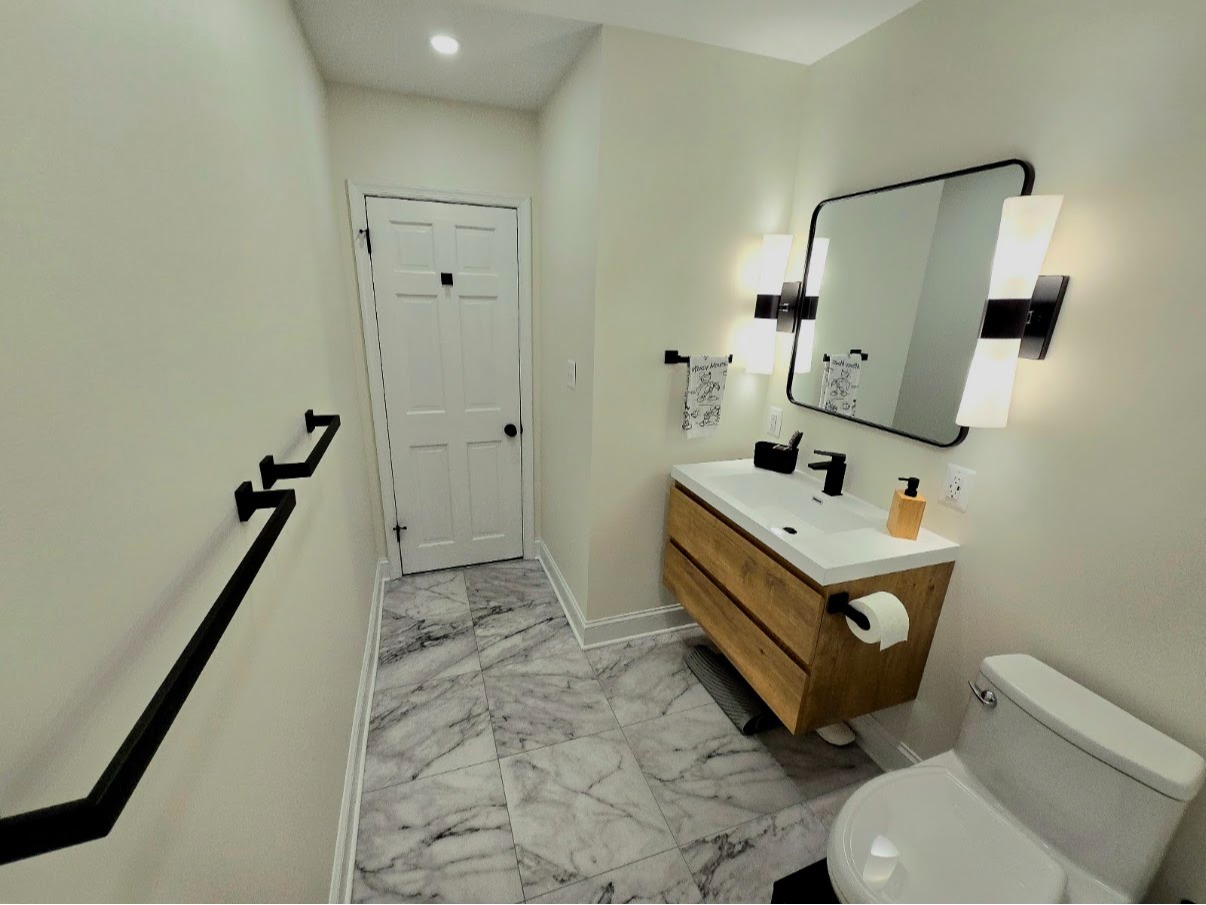 Remodeled bathroom featuring a floating wood vanity, marble-look tile flooring, and modern black fix 