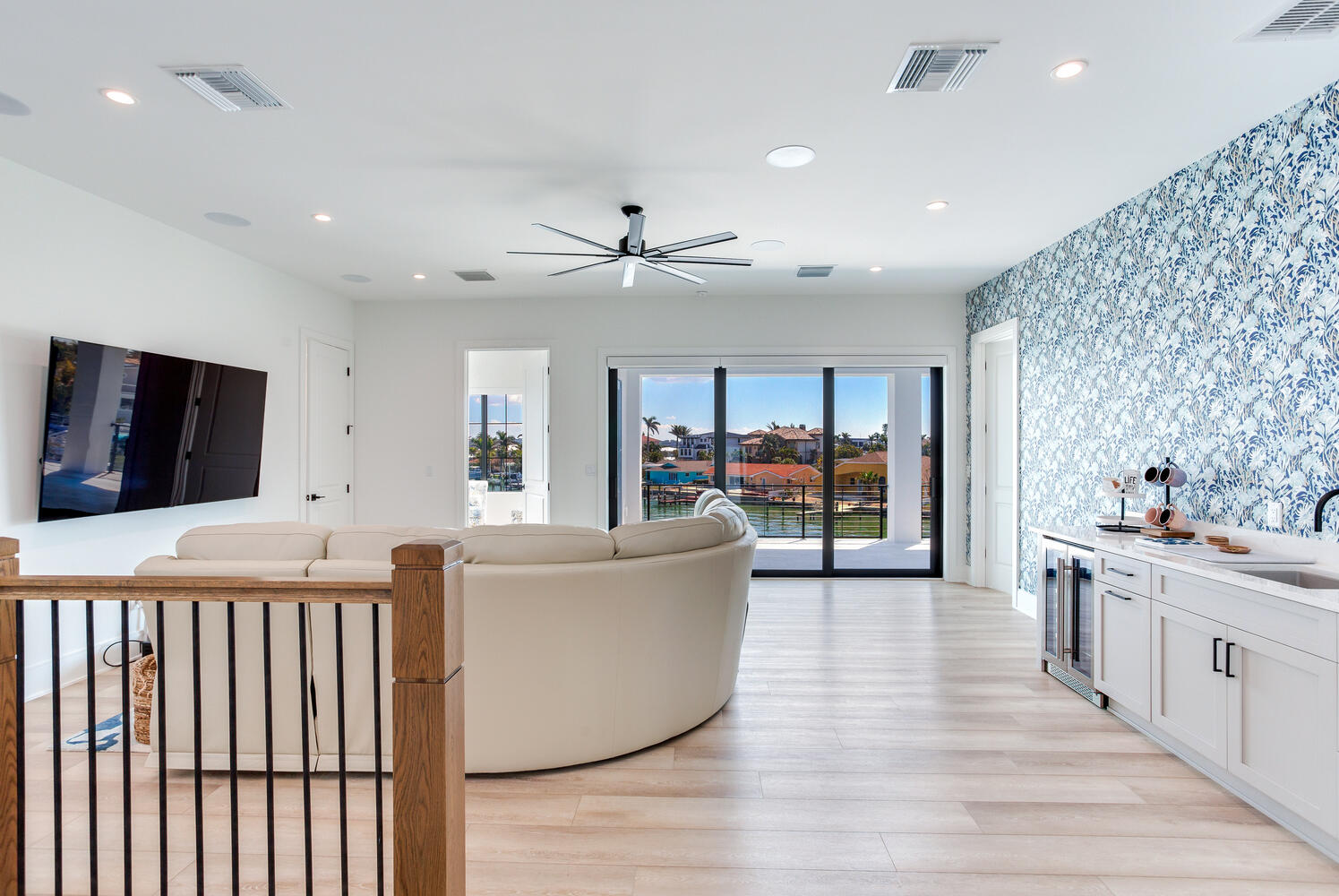 Bright open loft or living area with a built-in wet bar, patterned accent wall, wood railing, and modern coastal finishes.