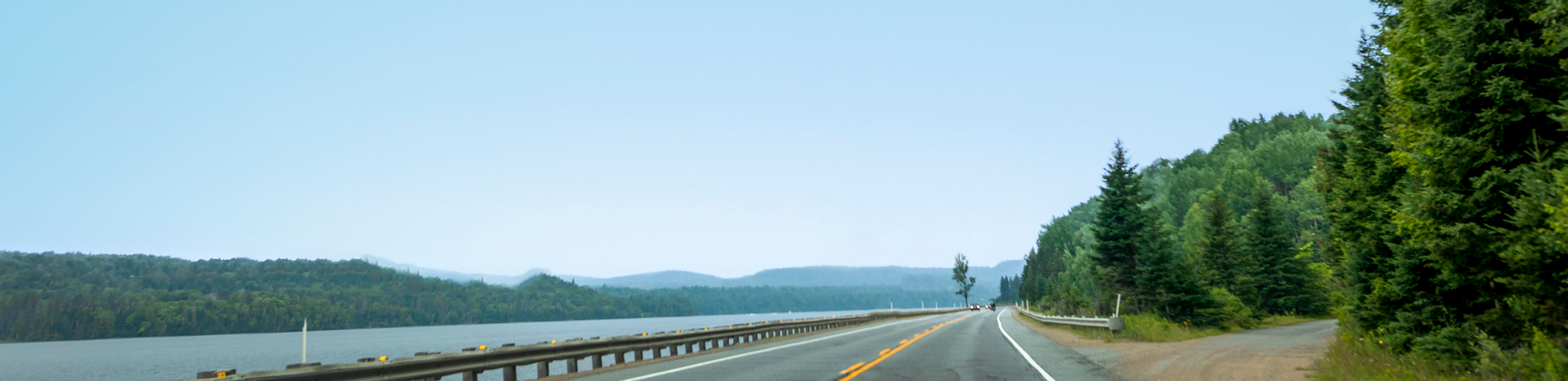 Open road with a river on one side and forest on the other.