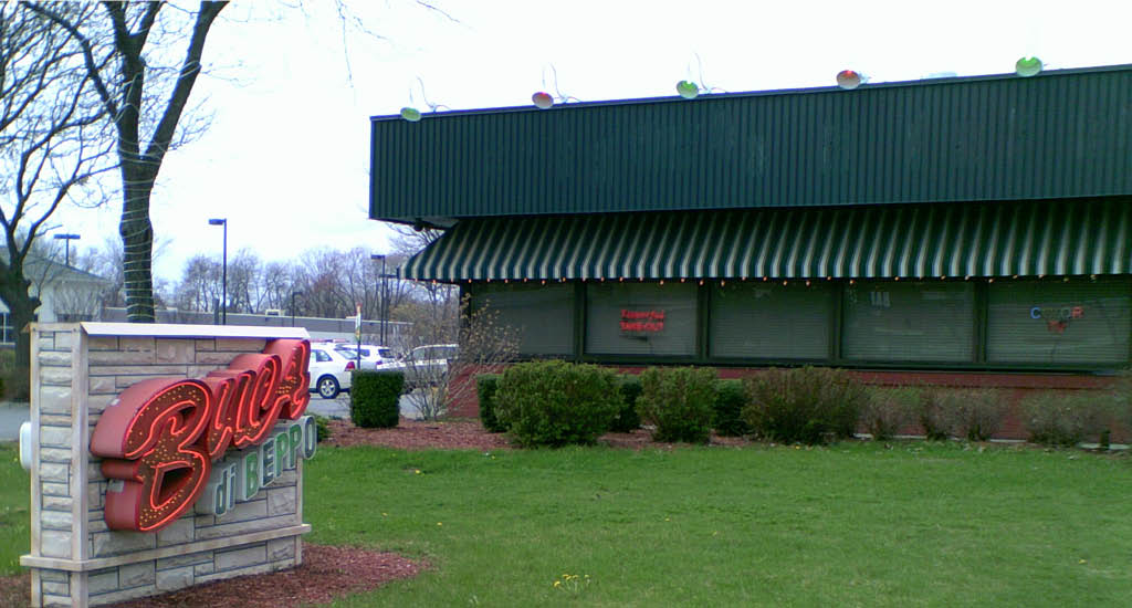 Buca di Beppo Albany featuring a brick road sign and a side view of the green restaurant walls.