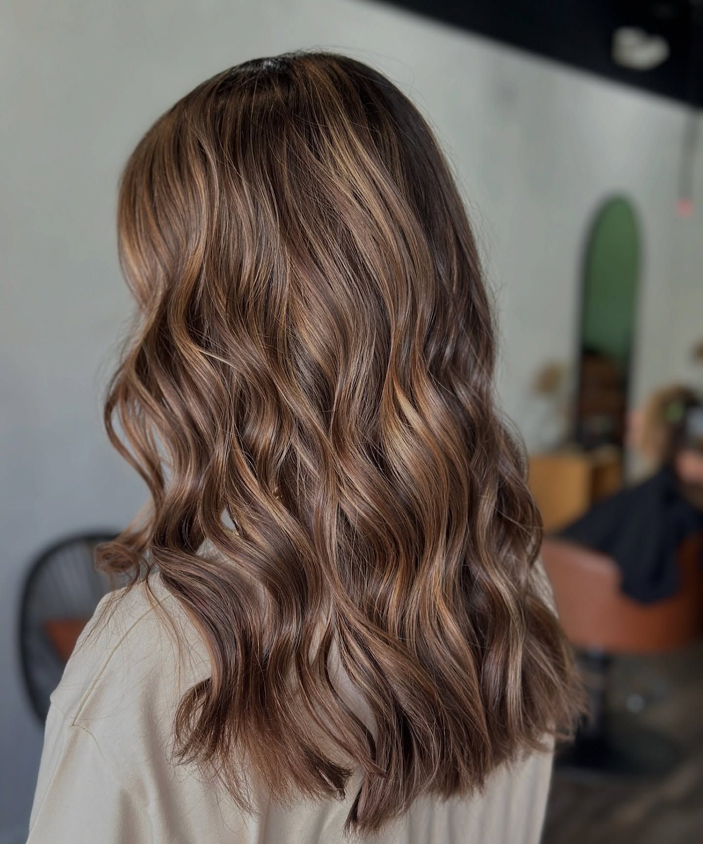 Side view of medium-length brown hair with soft waves and subtle highlights, professionally styled to create natural shine and movement.