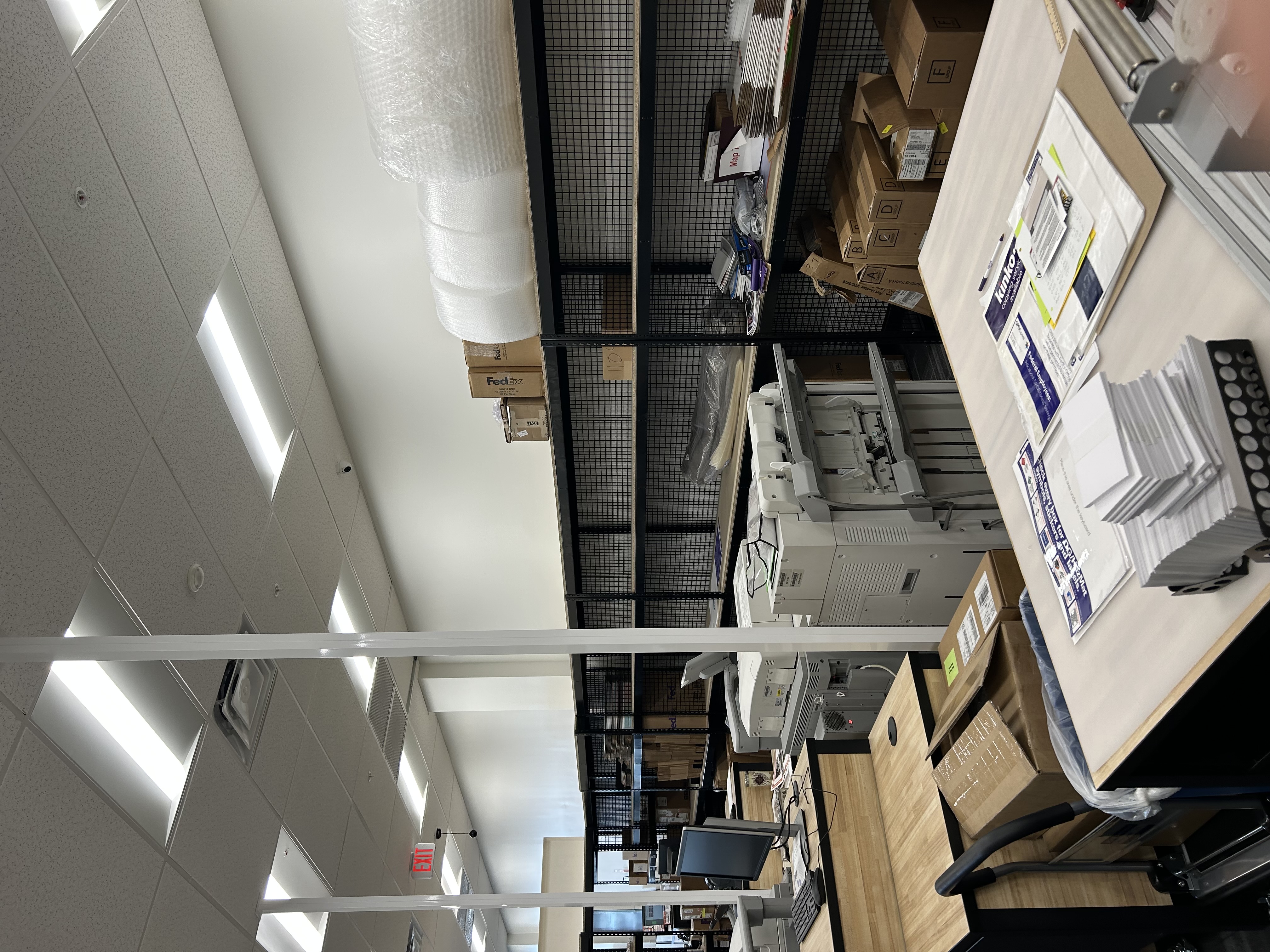Back-of-store print production area at FedEx Office North Miami FL with paper inventory, supplies, and printing equipment.