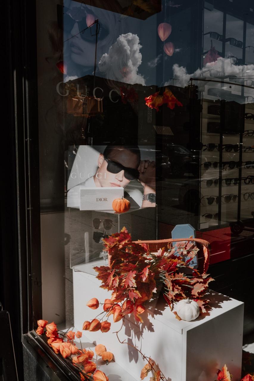 TK Optometry Brooklyn storefront window with designer sunglasses, Gucci and Dior displays, and autum 