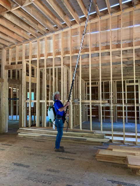 Pest control technician applying treatment inside new construction framing for termite prevention